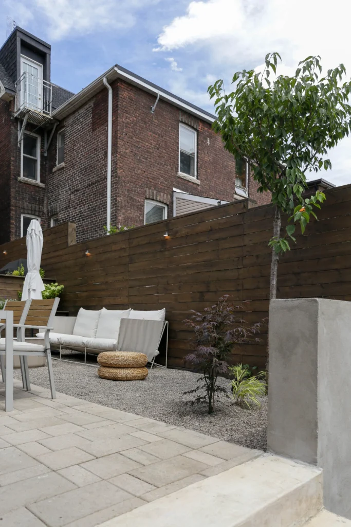 Backyard landscaping detail with gravel ground cover, ornamental trees, modern wood privacy fence, and integrated landscape lighting in Toronto