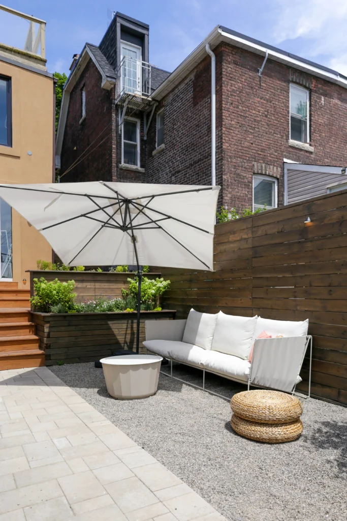 Backyard landscaping detail with gravel ground cover, ornamental trees, modern wood privacy fence, and integrated landscape lighting in Toronto