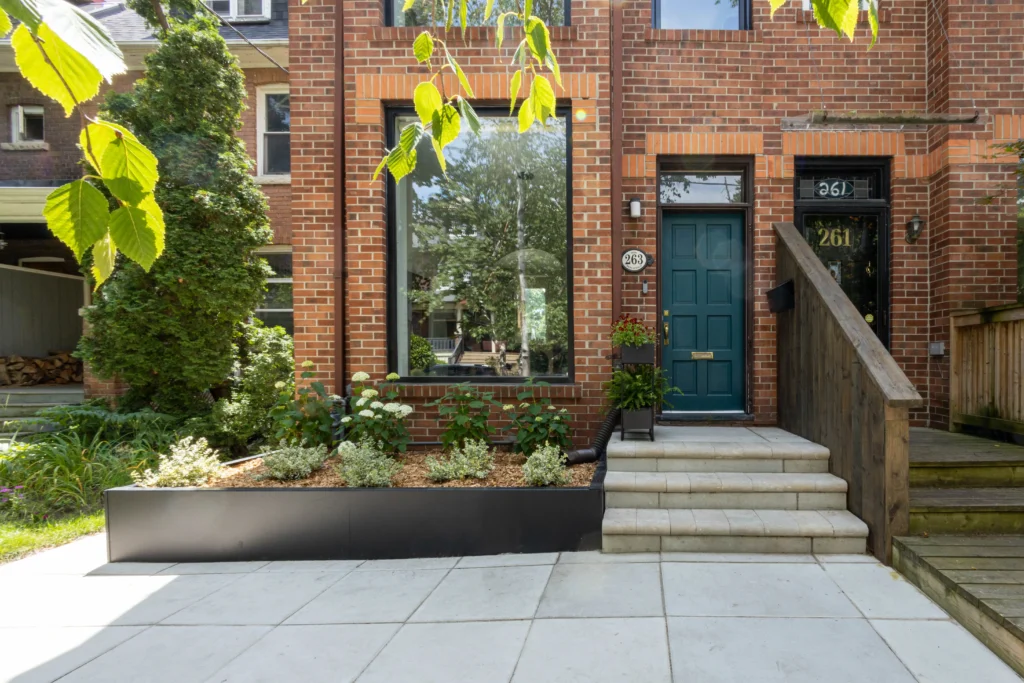 Front yard landscaping in Toronto with raised planter bed, mature tree, modern stone walkway, and soft landscape lighting in front of brick home