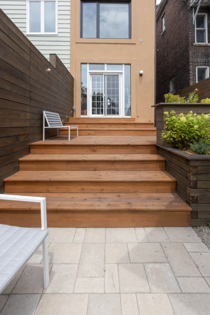 Multi-level backyard cedar deck with wide steps, modern privacy fencing, built-in planter, and patio stone base in Toronto