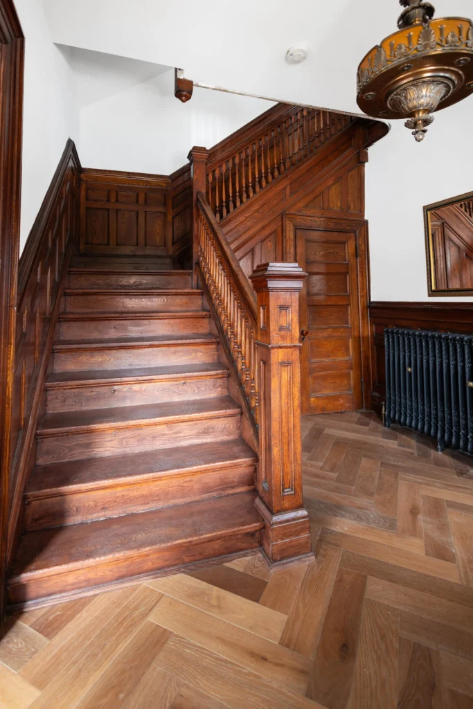 Restored Victorian staircase in Toronto home with original wood detailing, paneling, and herringbone flooring