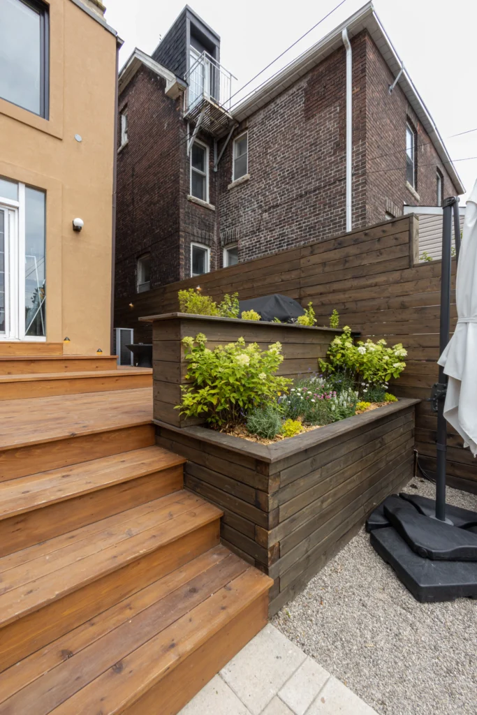 Multi-level backyard cedar deck with wide steps, modern privacy fencing, built-in planter, and patio stone base in Toronto