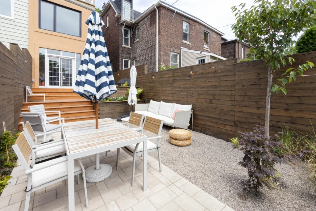Modern backyard patio in Toronto with interlocking stone, gravel lounge area, cedar privacy fence, outdoor seating, and striped umbrella dining setup