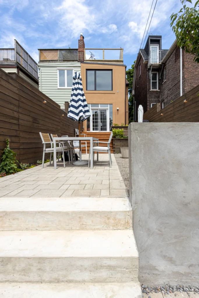 Multi-level backyard design with concrete steps, interlocking stone patio, cedar privacy fencing, and raised deck in Toronto