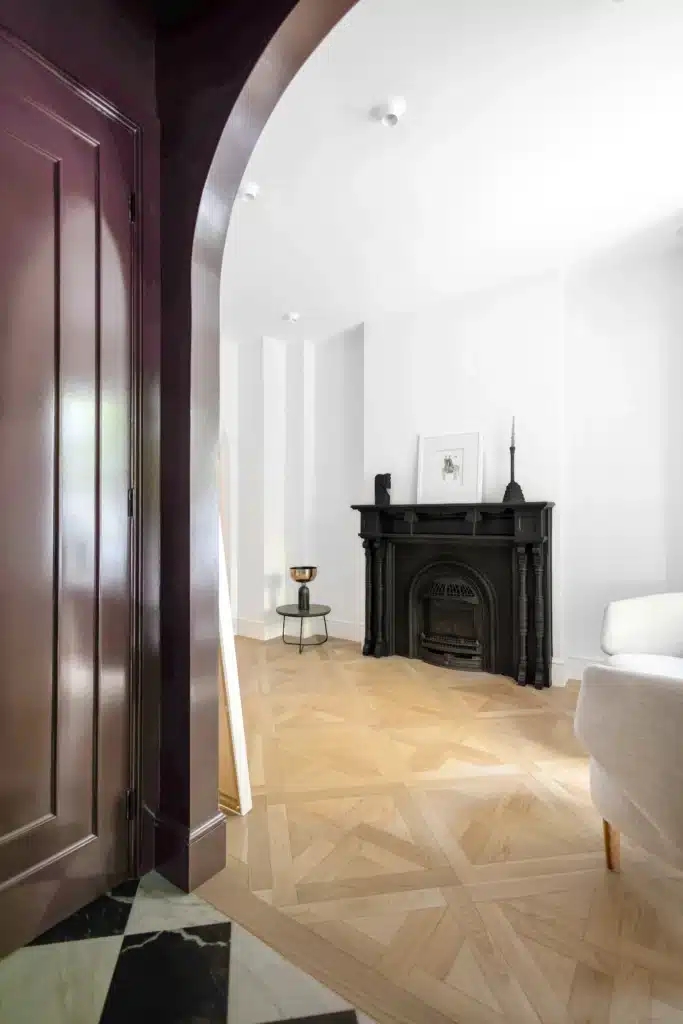 Renovated home entryway with a deep burgundy arched alcove, black glass front door, black-and-white checkerboard floor, and light wood flooring.