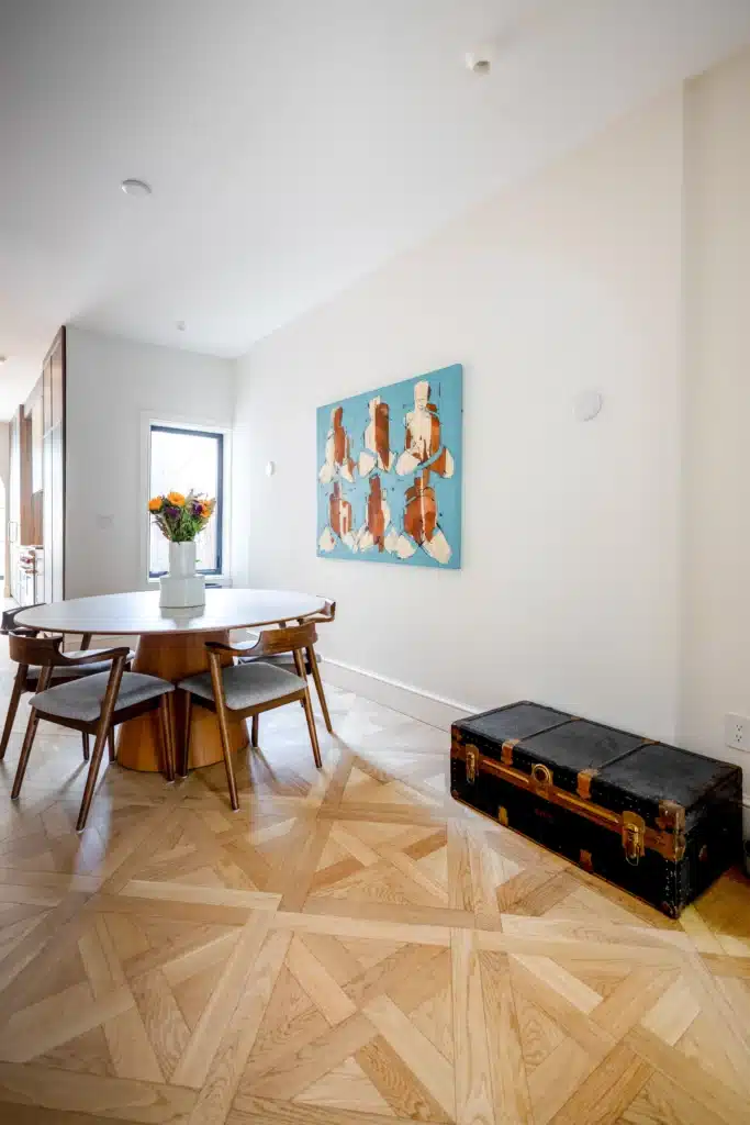 Renovated dining area with an oval table, patterned wood floor, and staircase beside an archway leading to a bright sitting room.