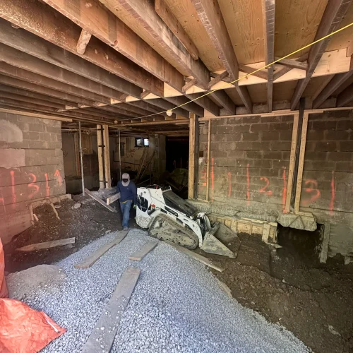 Basement underpinning in progress at a Toronto home — excavated floor, numbered foundation sections, and a Bobcat skid steer removing soil during a dig-down project by TMDC Group