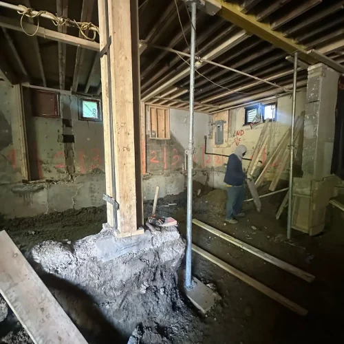 TMDC Group contractor working inside a Toronto basement during underpinning — temporary support posts, concrete column footings, and sequenced foundation walls visible during dig-down excavation