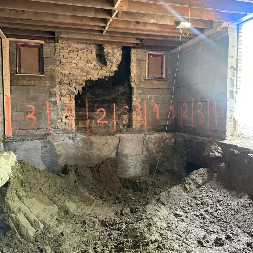 TMDC Group contractor working inside a Toronto basement during underpinning — temporary support posts, concrete column footings, and sequenced foundation walls visible during dig-down excavation