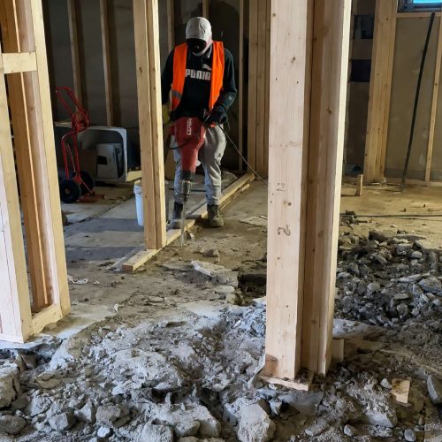 Basement underpinning construction worker using a jackhammer to break concrete floor during residential basement lowering and foundation renovation in Toronto.