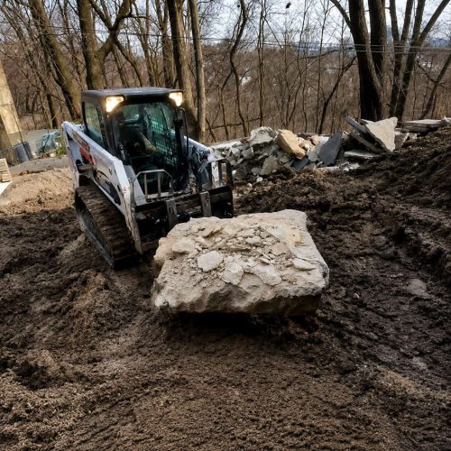 Toronto underpinning excavation project with skid steer loader removing concrete and soil during residential basement lowering construction outdoors.